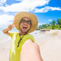 Handsome man having fun taking a selfie at the beach on holiday